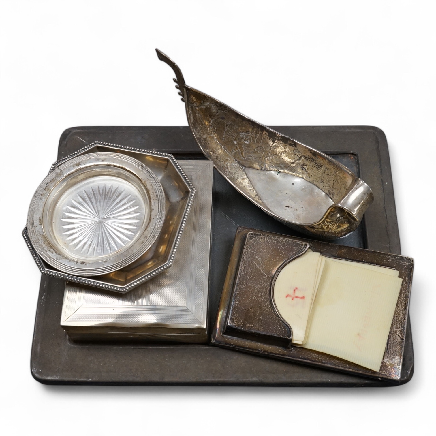 A 1940's silver mounted cigarette box, two small silver dishes, a silver mounted desk calendar, a silver mounted photograph frame and a continental silver bonbon dish modelled as a boat, import marks for John George Pidd